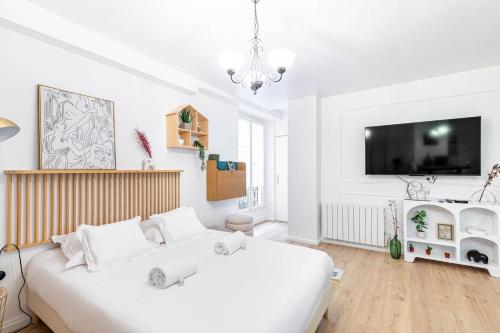une chambre blanche avec un grand lit et une télévision à écran plat dans l'établissement GuestReady - Studio près de République pour Deux, à Paris