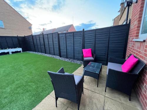 a patio with two chairs and a table with pink pillows at Spacious 4 Bedroom, 3 Bath House by Jesswood Properties Contractors, Business and Leisure with Free Parking and WIFI in Peterborough