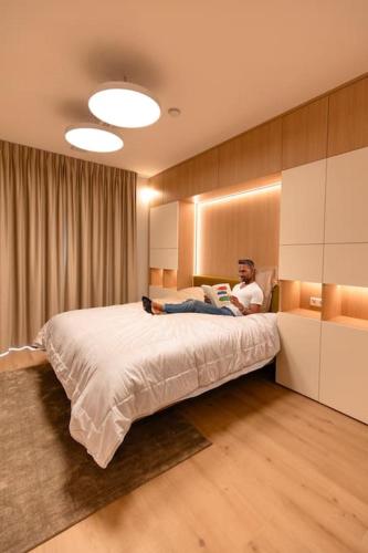 a man sitting on a bed reading a book at Henry's Appt with a private Suite 412 - Shared kitchen in Luxembourg