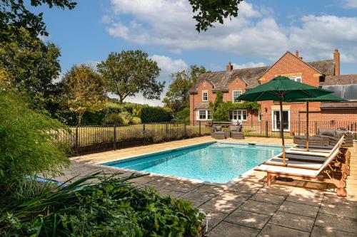 a swimming pool with a green umbrella and chairs and a house at Port Hill House in Medbourne