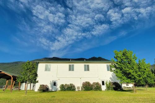 una gran casa blanca con árboles en un campo en Charming Chalet Close to GNP, Downtown & Game Room!, en Columbia Falls