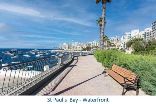 a park bench on a walkway near the water at Ta' Pace, Holiday Apartment in St Paul's Bay