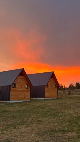 two barns in a field with a sunset in the background at NORTH VILLAS Žabljak in Žabljak