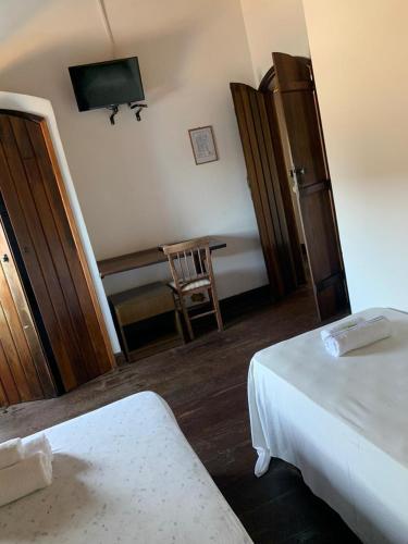 a room with two beds and a desk with a television at Solar Colonial Pousada in Iguape