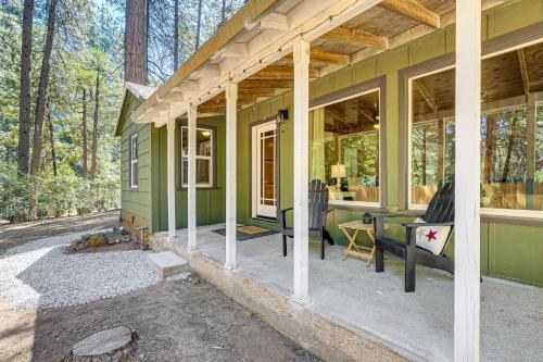 a green house in the woods with a porch at Walk to Winery Cozy Cabin with Fire Pit in Murphys in Murphys