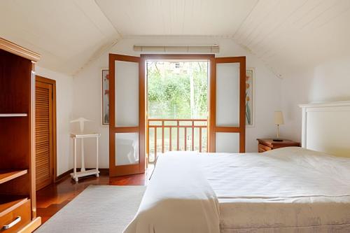 a white bedroom with a bed and a window at Apartamentos Centrinho Capivari - Recanto Boticário in Campos do Jordão
