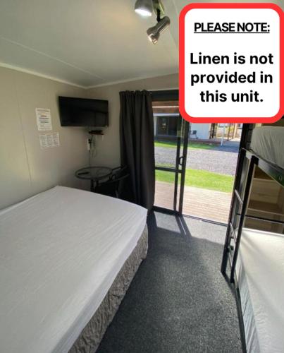 a room with a bed with a sign that readslinear is not provided in this at Sapphire Springs Holiday Park and Thermal Pools in Katikati