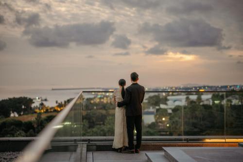 a bride and groom standing on a balcony looking at the sunset at JW Marriott Jeju Resort & Spa in Seogwipo