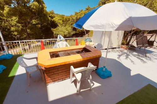 a patio with an umbrella and chairs and a fireplace at 星光の城 船でアクセス友人との集まりに最適なリラックスできる秘境 in Hinase
