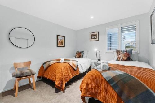 a bedroom with two beds and a mirror and a chair at Wanaka Station Apartment in Wanaka