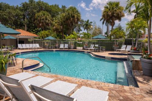 a swimming pool with chairs and tables and trees at SpringHill Suites Fort Lauderdale Airport in Dania Beach