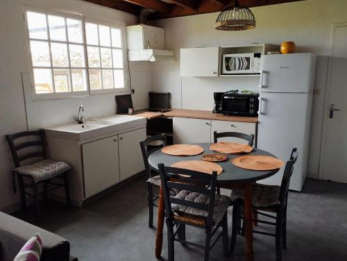 une cuisine avec une table avec des chaises et un réfrigérateur dans l'établissement La maisonnette 2personnes le rdc à 1200m de la mer, à Agon-Coutainville