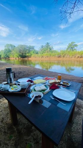 a picnic table with plates and utensils next to a river at River paradise safari house with cooking class in Udawalawe
