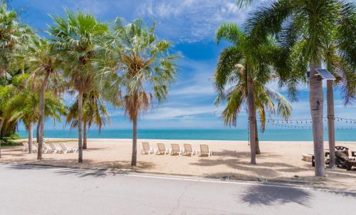 a beach with chairs and palm trees and the ocean at Beachfront Apartment with Balcony, Sea View & Pool View - Cha Am - Hua Hin in Ban Pak Khlong Cha-am