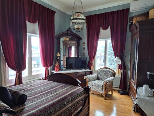 a bedroom with a bed and a chair and windows at Gîte au Charme Victorien in Beauceville