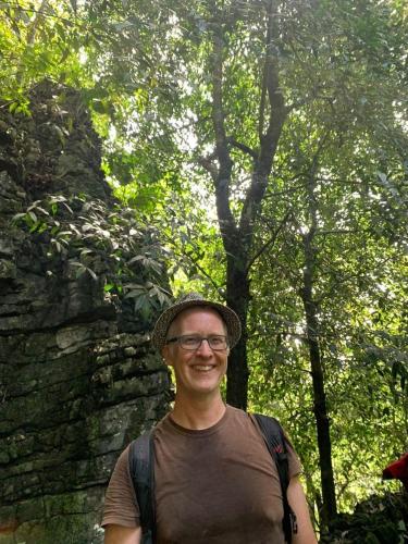 a man wearing a hat standing in front of a tree at Wisma Batu Mandi in Bukit Lawang