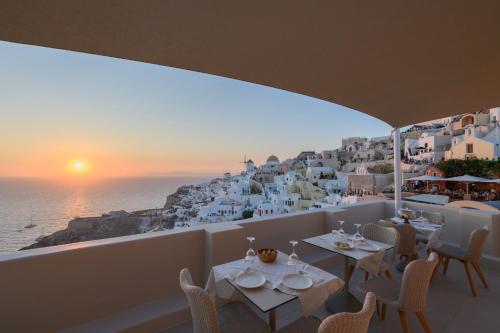 a restaurant with white tables and chairs and a view of the ocean at Art Maisons Oia Castle in Oia