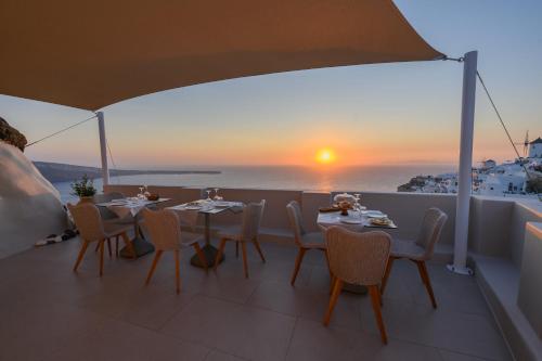 a table and chairs on a balcony with the sunset at Art Maisons Oia Castle in Oia