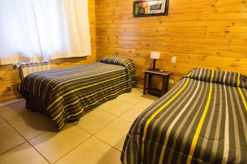 two beds in a room with wooden walls at Encanto del Rio in Villa La Angostura
