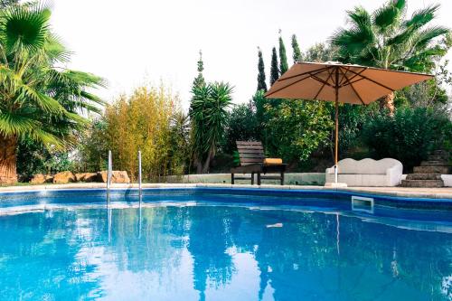 a blue swimming pool with an umbrella and a chair at Quinta dos Cochichos - Country Houses in Olhão