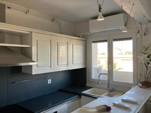 une cuisine avec des armoires blanches, un évier et une fenêtre dans l'établissement Appartement F3 proche de la mer, à Cagnes-sur-Mer
