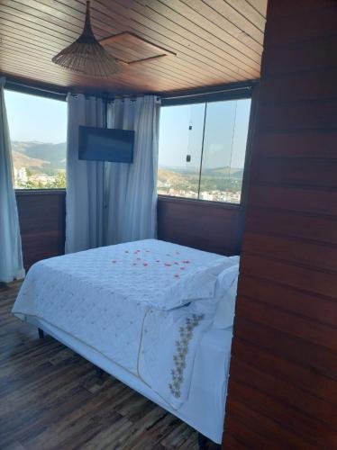 a bedroom with a bed with white sheets and windows at Pousada Chalezinho - Suite Crepúsculo in Santa Rita do Sapucaí