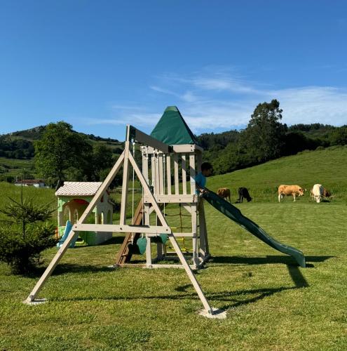 a boy playing on a slide in a field with cows at Apartamentos la Roblera in Oreña