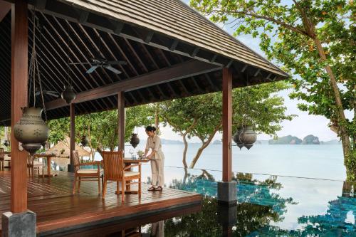 a woman standing at a table on a deck next to the water at Phulay Bay, A Ritz-Carlton Reserve in Tab Kaek Beach