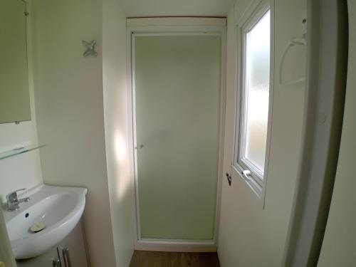 une salle de bain blanche avec un lavabo et une fenêtre dans l'établissement Mymobilhome 2 chambres Saint-Jean-de-Monts, à Saint-Jean-de-Monts