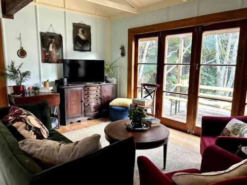 ein Wohnzimmer mit Sofa und Fernseher in der Unterkunft Oakura Pond Cottage - A unique kiwi holiday Bach in Oakura