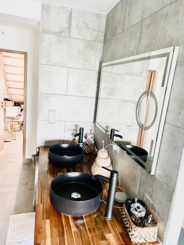 La salle de bains est pourvue de 2 lavabos noirs et d'un miroir. dans l'établissement Villa les cèdres piscine nature, à Fabrègues