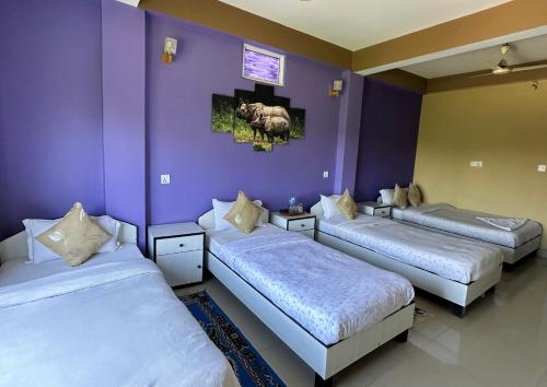 three beds in a room with purple walls at Hotel Rhinoceros-Homestay in Sauraha