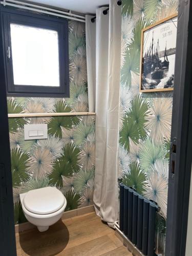 une salle de bain avec toilettes et un papier peint tropical dans l'établissement Maison 7 couchages & jaccuzi, à Étaples