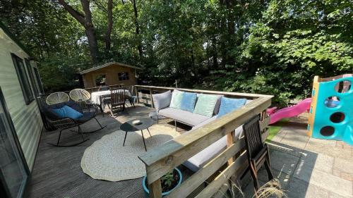 a deck with a couch and a table and chairs at SAYANG26 gezellige gezinsvriendelijke stacaravan op familiecamping De Vossenburcht in natuurgebied Reestdal - no workers allowed in IJhorst