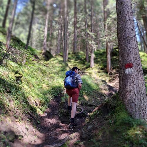 a man with a backpack walking on a trail in the woods at Hotel Pinzger Tux in Tux