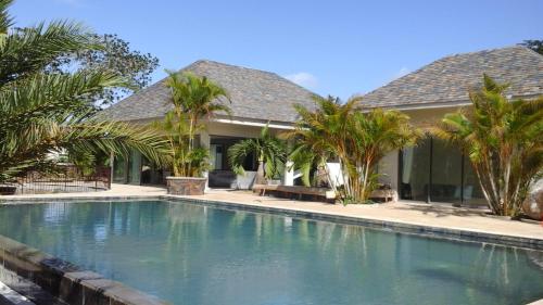 a swimming pool in front of a house with palm trees at La VILLA MAELA GOLF ANAHITA in Beau Champ