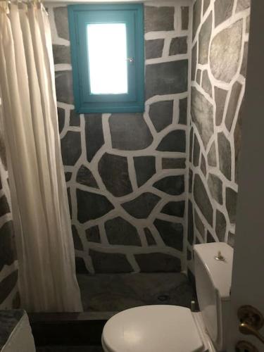 a bathroom with a toilet with a window and a wall at TaVLaDo Cycladic house in Serifos Chora