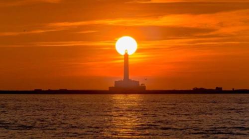 a sunset over the water with a lighthouse at La Corte dei Sarti in Copertino