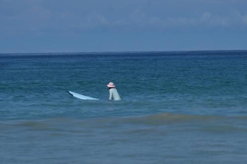 a person in a hat sitting on a surfboard in the ocean at Coco Mountain View Guest House Hotel in Kata Beach