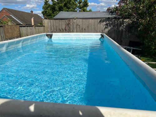 a large blue swimming pool in a backyard at Lavender Lodge - Pool and Hot Tub with sunset views over open fields in Wymondham