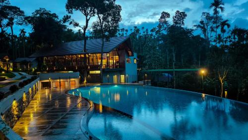 a swimming pool in front of a house at night at Sterling Lontano Waterfront Wayanad in Meppādi
