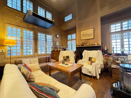 a living room with couches and a table and windows at Country Inn Orchard House in Hokuto