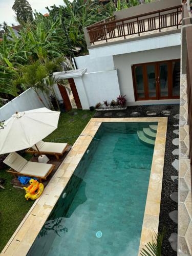 a swimming pool with two chairs and an umbrella next to a house at Nyoman House in Tabanan