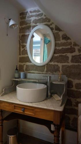 La salle de bains est pourvue d'un lavabo et d'un miroir sur un mur en pierre. dans l'établissement Chez Audrey & Fabien - Appartement avec terrasse, à Saint-Pantaléon-de-Larche