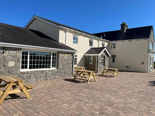 a patio with two picnic tables and a building at Ty Dderw Country Inn in Moelfre