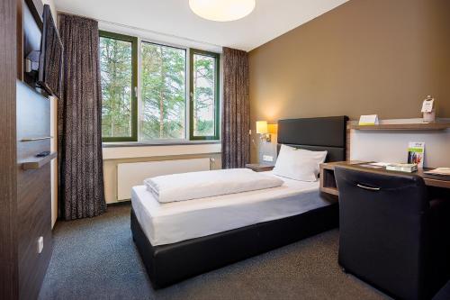 a hotel room with a bed and a desk and window at GenoHotel Forsbach in Rösrath