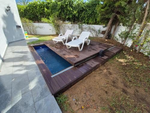 a wooden deck with two chairs and a pool at Maison moderne avec Piscine et accès plage - Résidence Jinen Hammamet in Hammamet Sud