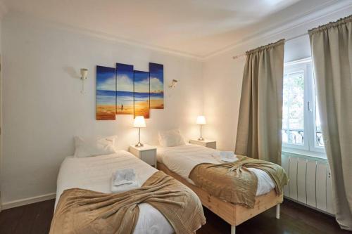 two beds in a room with two lamps and a window at Central Oasis Apartment in Cascais