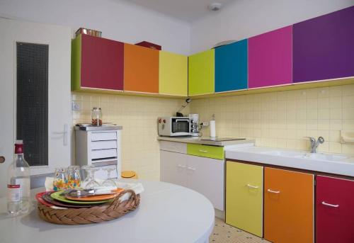 eine Küche mit bunten Schränken und einem Tisch mit einem Korb in der Unterkunft À 2 pas de plage et commerces, jardin & parking in Les Sables-dʼOlonne