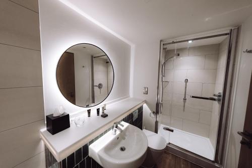 Un baño blanco con lavabo y espejo. en Reserve, by Warner Hotels - Heythrop Park, en Chipping Norton